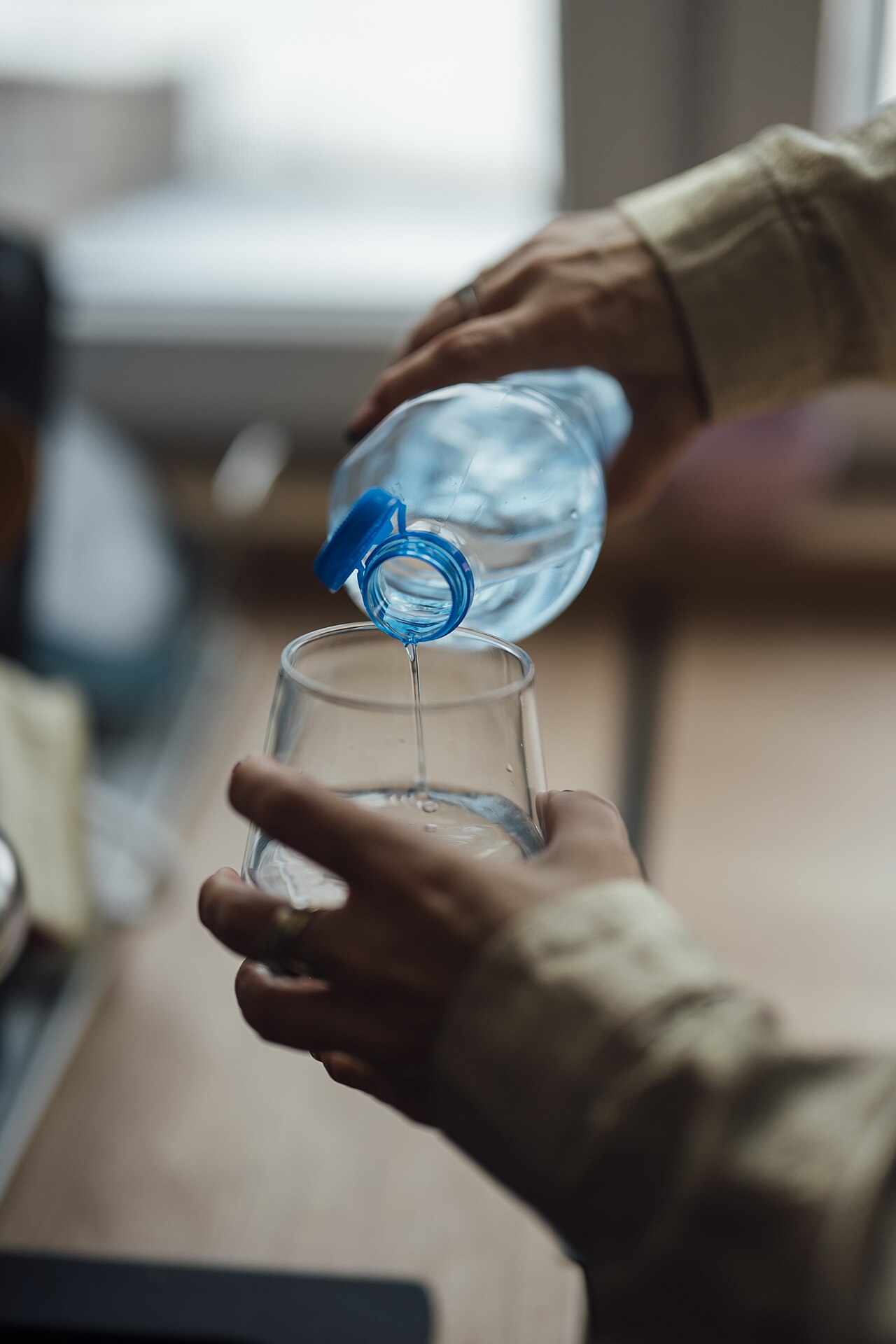 Hands pouring water from a bottle into a drinking glass