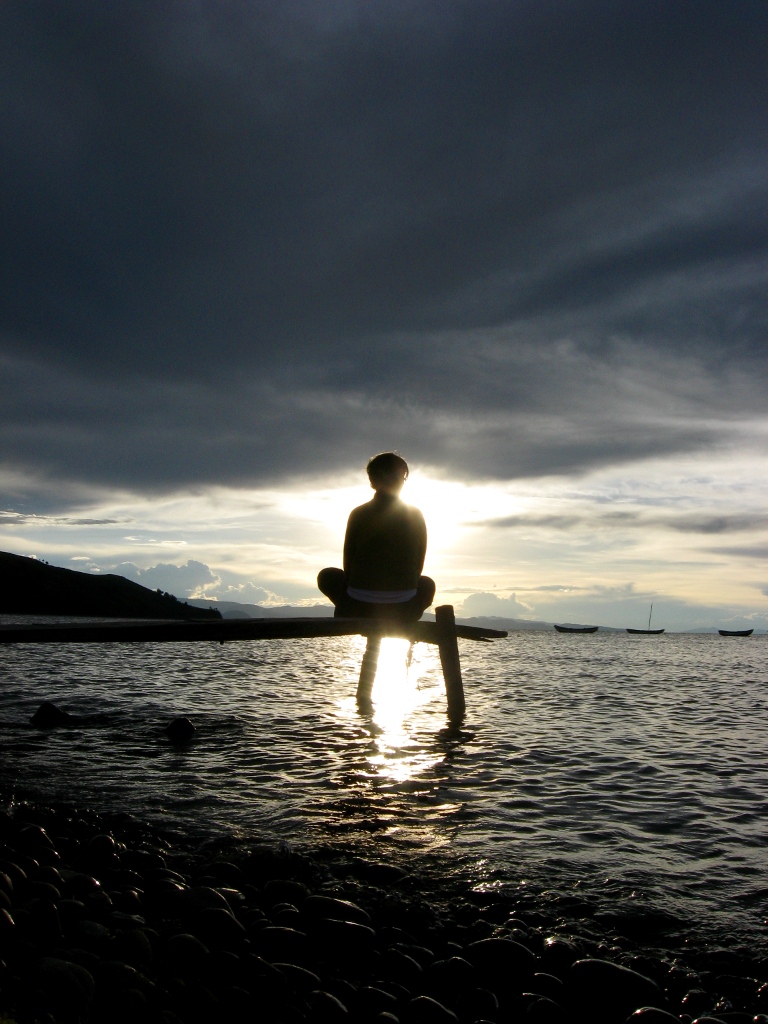 Person meditating cross-legged in silhouette beside Lake Titicaca